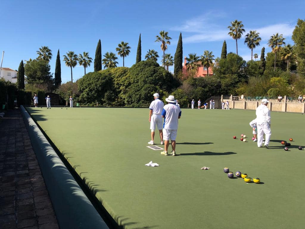 Match play on the Miraflores green under a blue sky, with palms and cypress trees